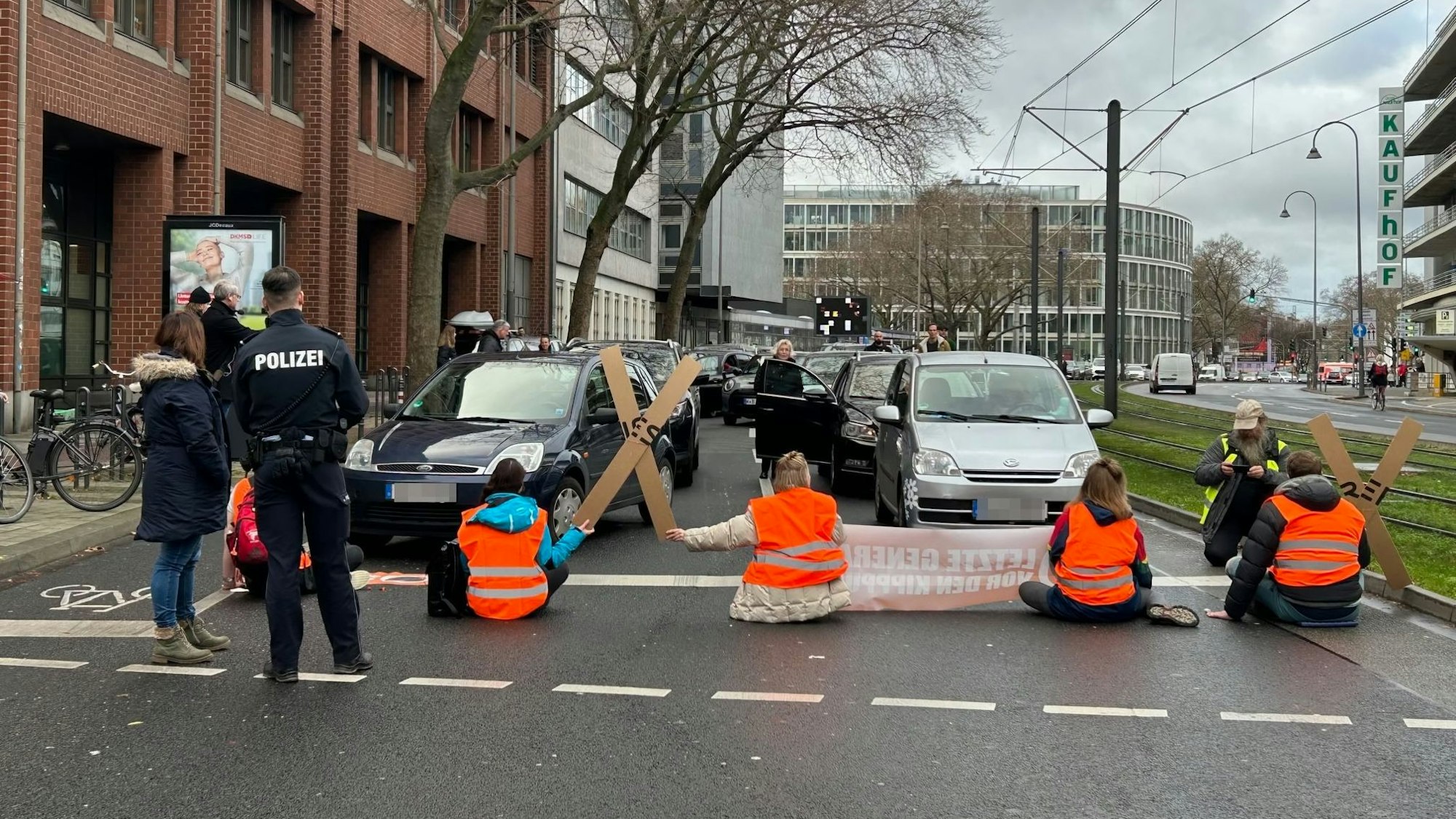 Aktivistinnen und Aktivisten der „Letzten Generation“ blockieren am Freitagmittag mit einer Sitzblockade die Cäcilienstraße, eine der zentralen Verkehrsachsen in der Kölner Innenstadt.