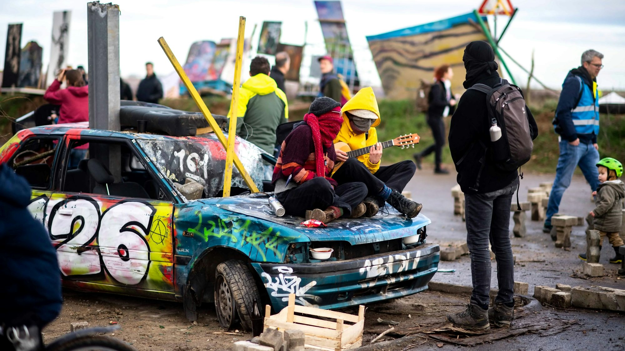 Auf einem kaputten Auto sitzen zwei Klimaaktivisten, die Musik machen.