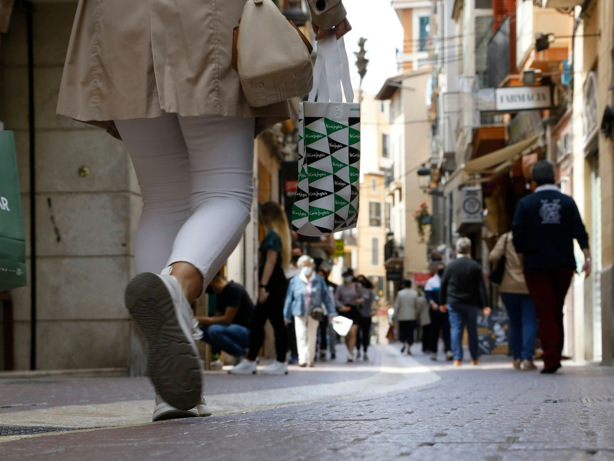 Kunden und Kundinnen mit Einkaufstüten gehen durch eine Einkaufsstraße in Palma auf Mallorca.