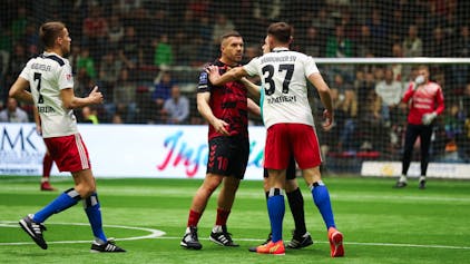 Lukas Podolski wird von einem Mann im weißen Trikot an der Schulter gefasst. Er schaut wütend.