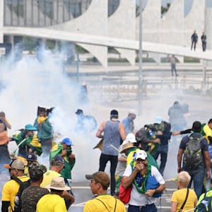 Menschen mit Kleidung in den Farben der Flagge Brasiliens stehen in dickem Rauch, einige halten sich Mund und Nase zu.
