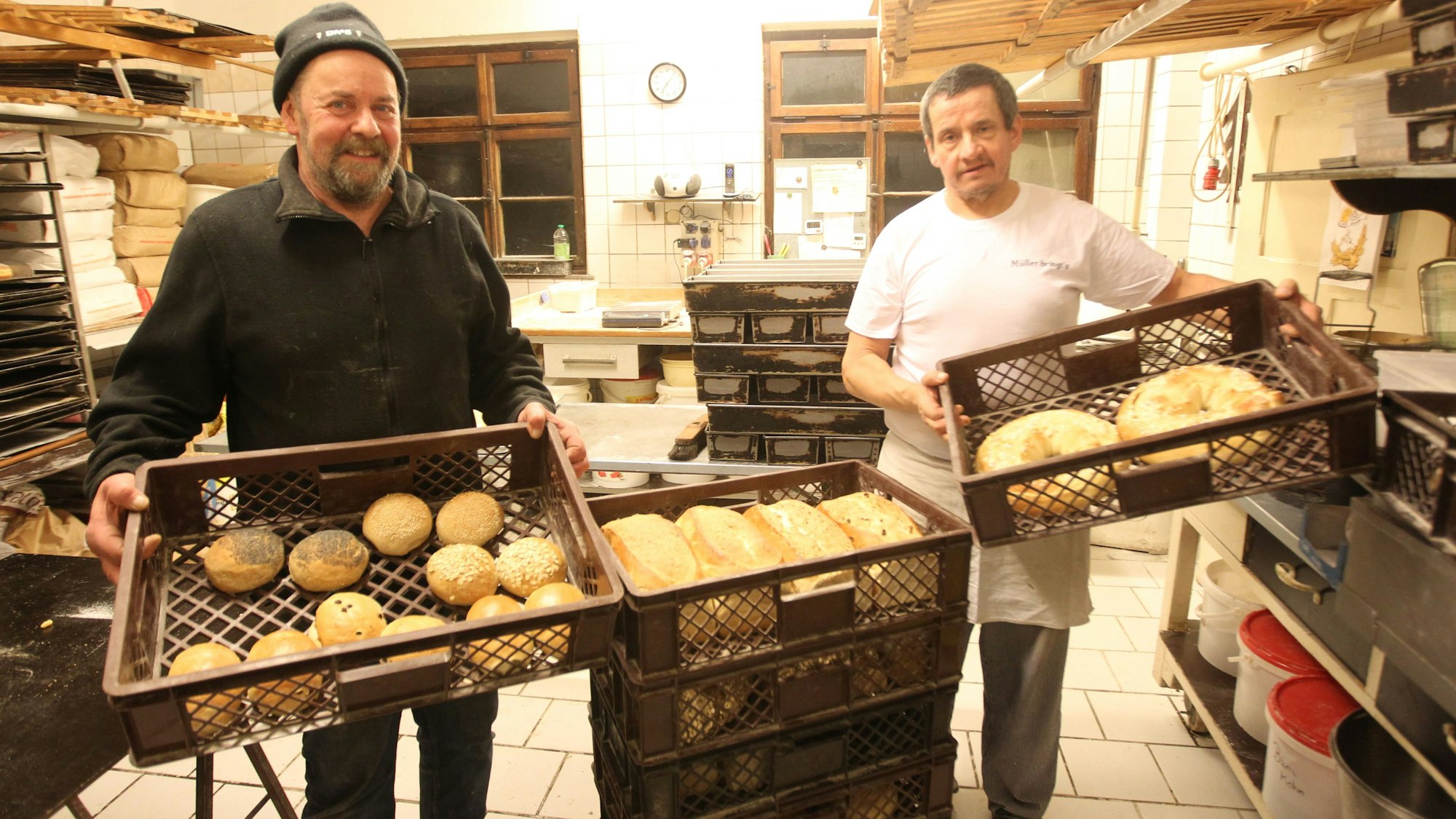 Zwei Männer zeigen in der Backstube der Gammersbacher Mühle Brot und Brötchen aus dem holzbefeuerten Steinofen.