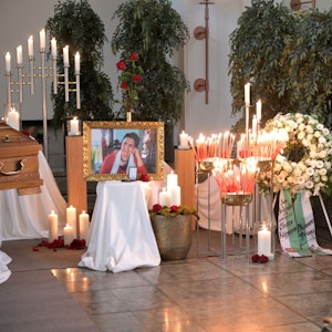 Blumen und Kerzen stehen neben dem Sarg und einem Bild von Philomena Franz.