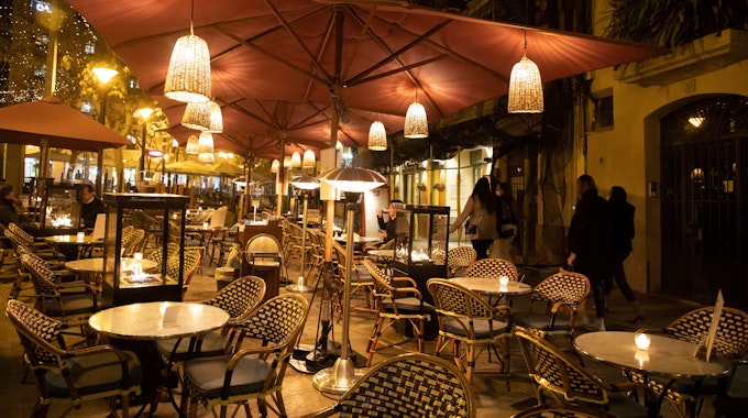 Das undatierte Symbolfoto zeigt den Außenbereich eines Restaurants mit Tischen, Stühlen und Laternen, die an Sonnenschirmen befestigt sind.