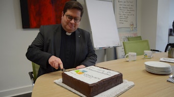 1Pfarrer Tobias Hopmann schneidet den Kuchen  an, der das Logo der neuen pastoralen Einheit Euskirchen zeigt.