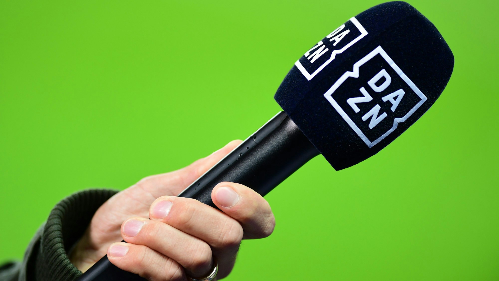 Die Hand eines Reporters hält bei einem Interview vor dem Spiel ein Mikrofon mit der Aufschrift DAZN. (Symbolbild)