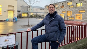 Thomas Heidbrink, der Schulpflegschaftsvorsitzender der GGS Hohe Straße steht am Zaun vor der Schule und lächelt.