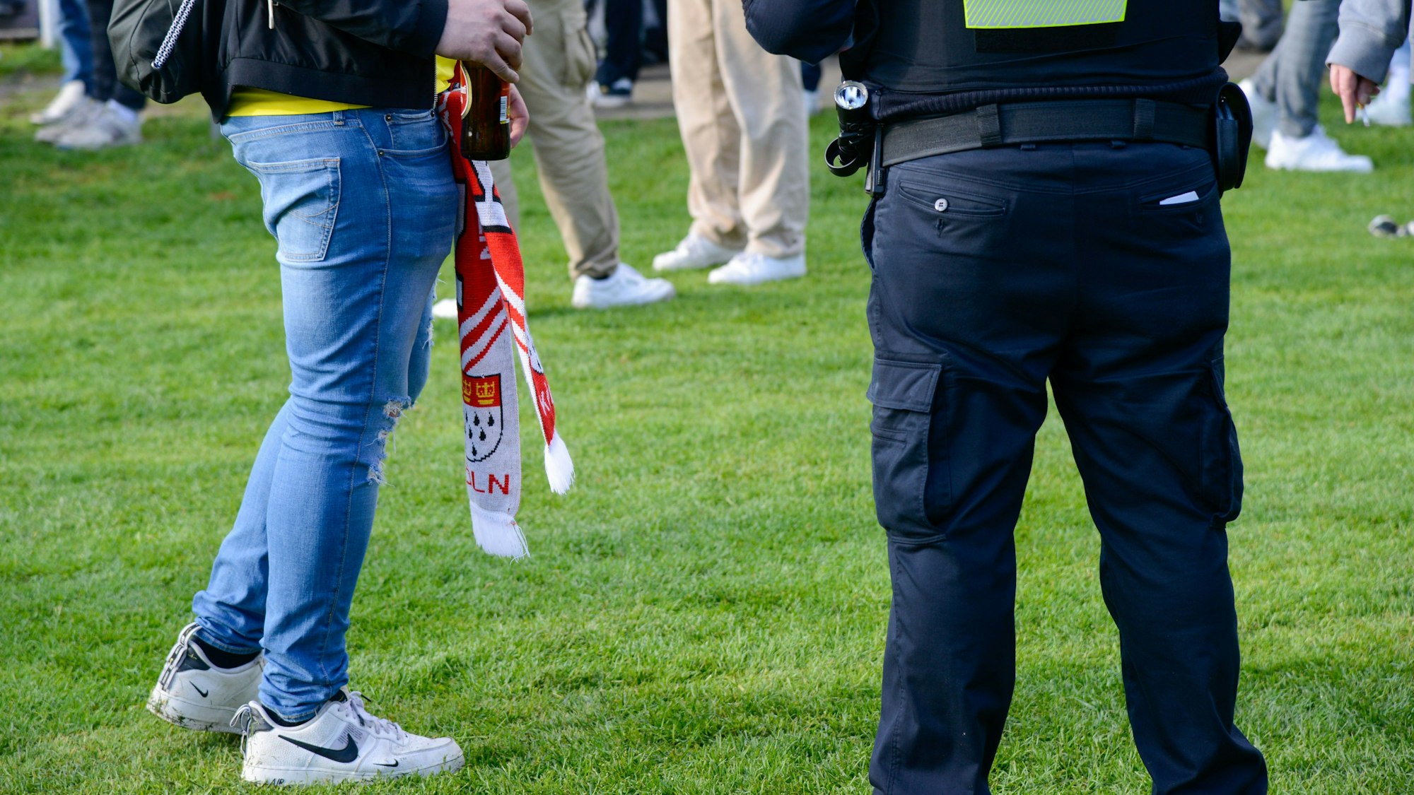 Ein FC-Fan steht auf den Jahnwiesen neben einem Beamten der Polizei.
