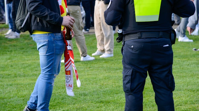 Ein FC-Fan steht auf den Jahnwiesen neben einem Beamten der Polizei.