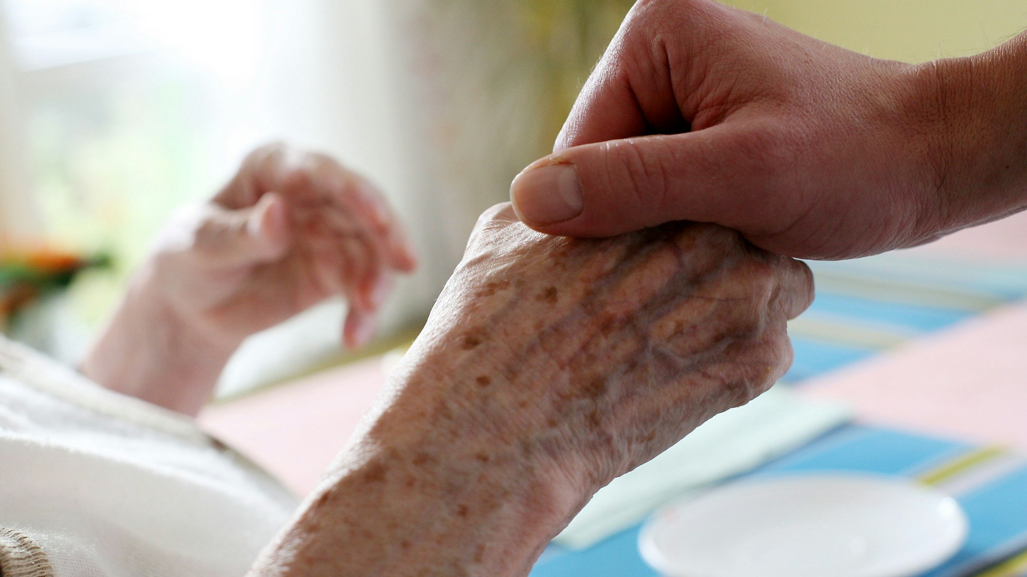 Ein Mitarbeiter eines Alten-und Pflegeheims hält die Hand einer Bewohnerin.