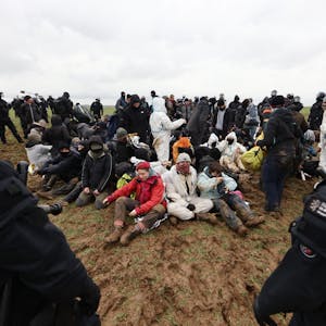 Polizisten und Klimaaktivisten auf einem Feld nahe der Abrisskante von Garzweiler II.Die Klimaschützer sitzen auf der Erde und sind von Sicherheitskräften umgeben.&nbsp;