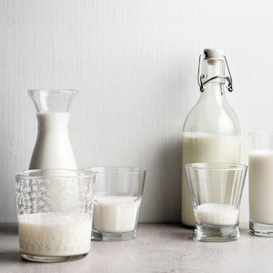 Links im Bild ist Milch in Gläsern und einer Flasche, während auf der rechten Seite Milchalternativen abgefüllt sind.