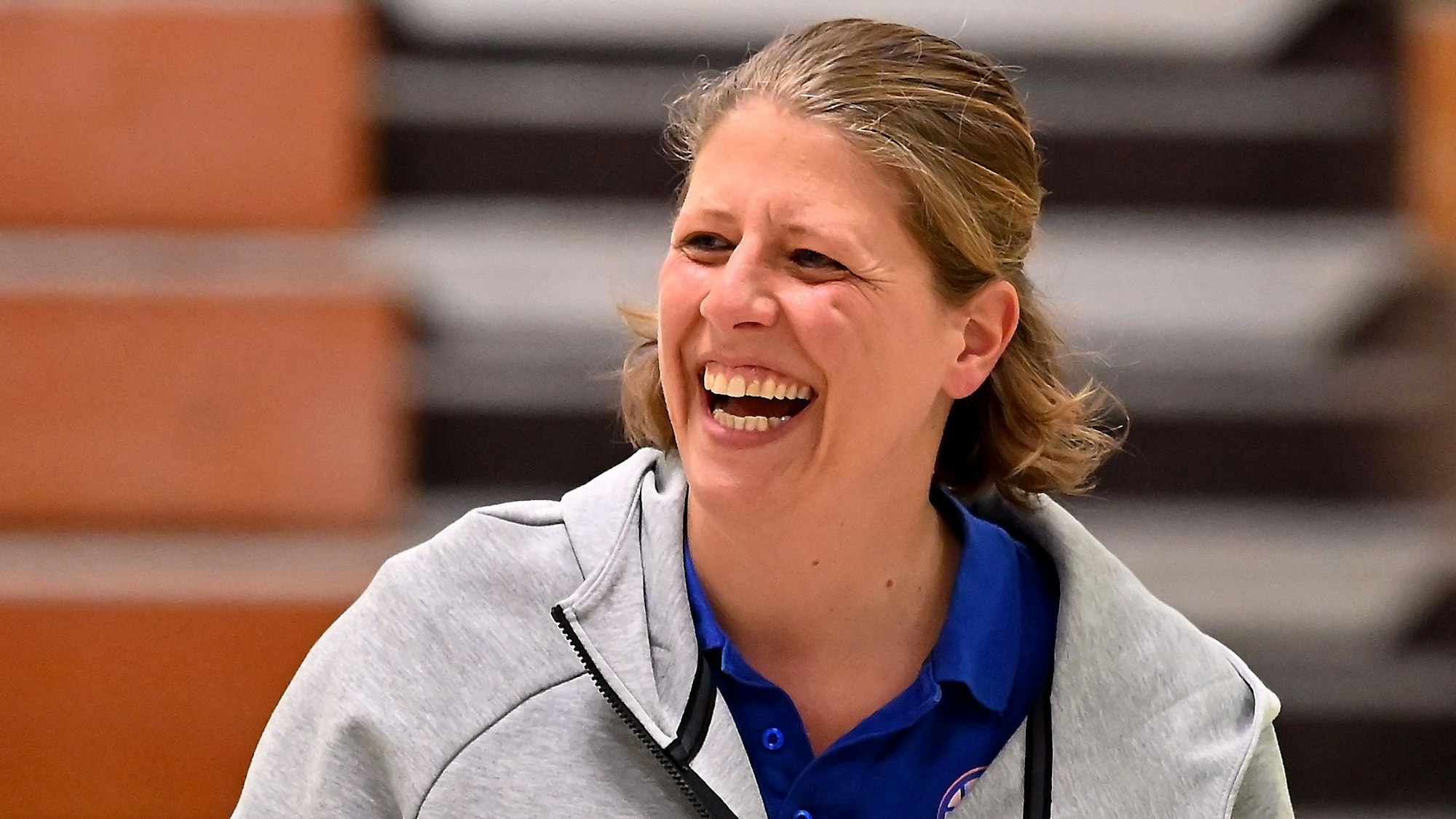 Eine Basketballtrainerin steht lachend am Spielfeldrand.