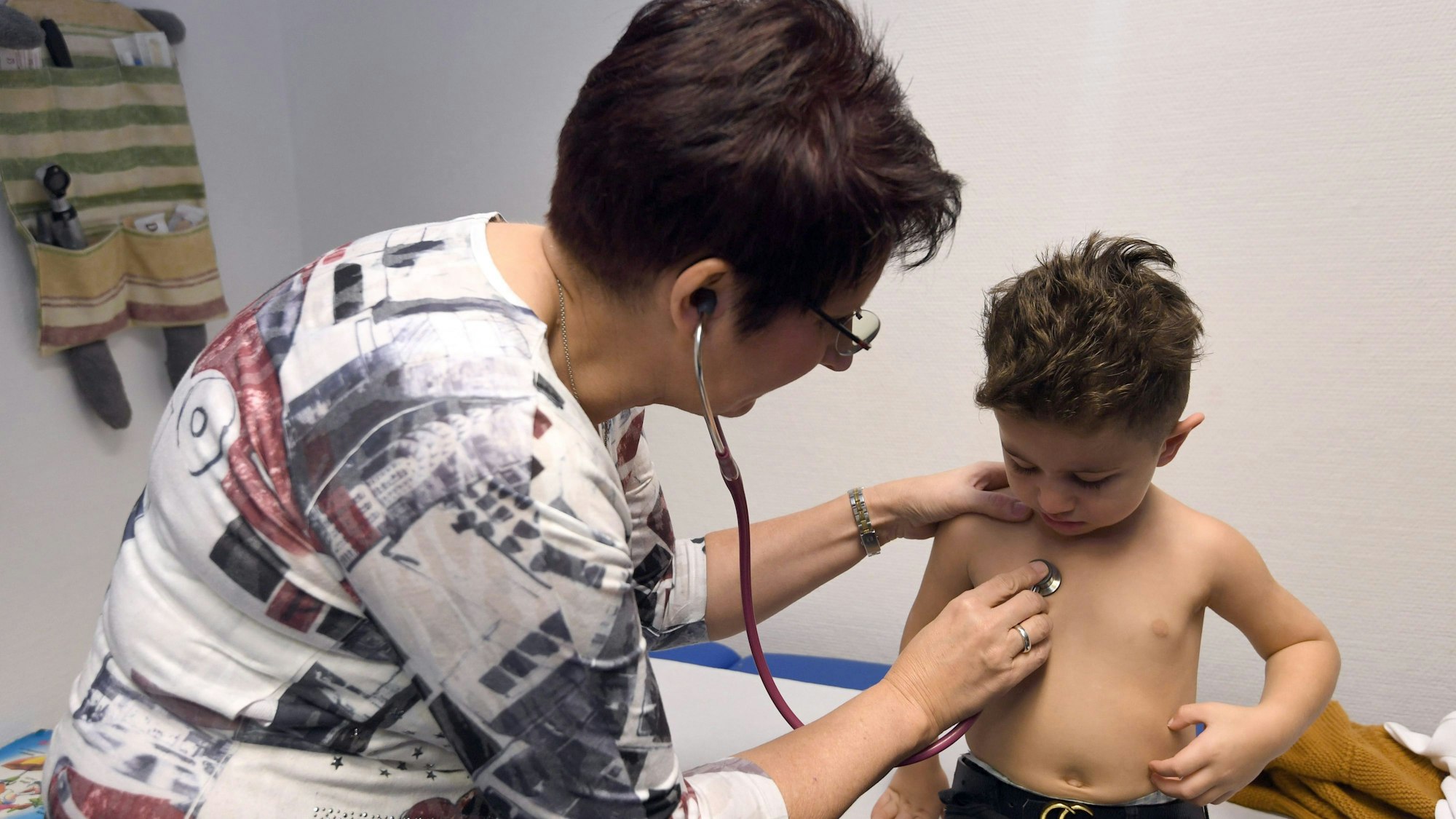 Eine Ärztin hört mit einem Stethoskop den Brustbereich eines kleinen Jungen ab.