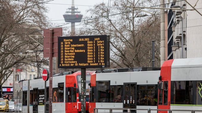 Eine Straßenbahn passiert die Haltestelle am Barbarossaplatz. Im Bildvordergrund befindet sich eine digitale Anzeigetafel mit Angaben zu den nächsten Bahnverbindungen.&nbsp;