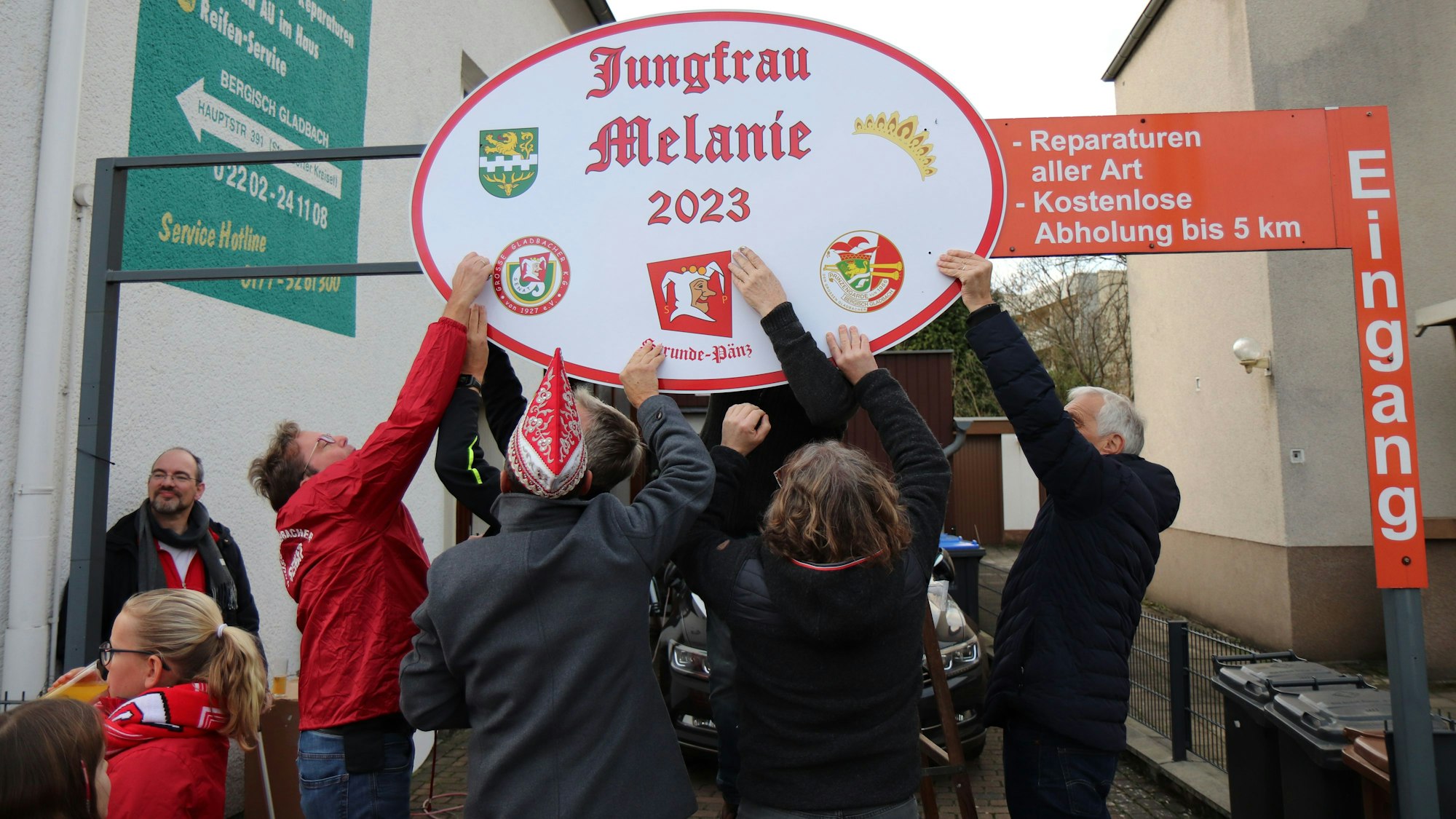 Karnevalisten bringen ein Schild mit der Aufschrift „Jungfrau Melanie 2023“ an.