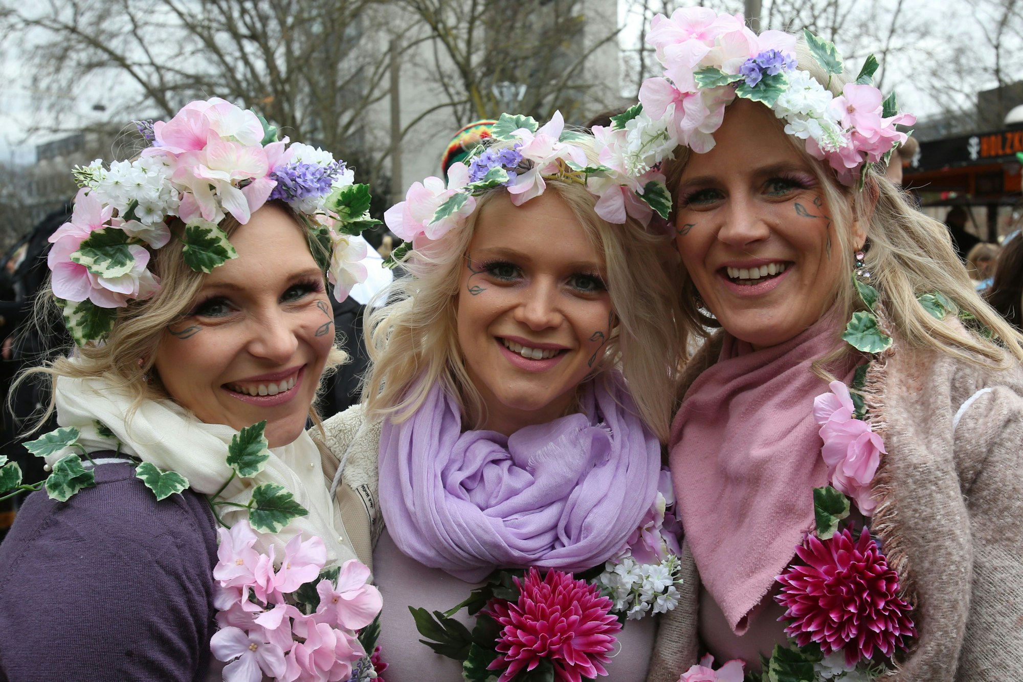 Drei junge Frauen mit rosa und lila Blumen im Haar. (Symbolbild)