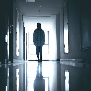 Eine junge Frau steht verlassen in einem dunklen Krankenhausflur.