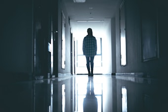 Eine junge Frau steht verlassen in einem dunklen Krankenhausflur.