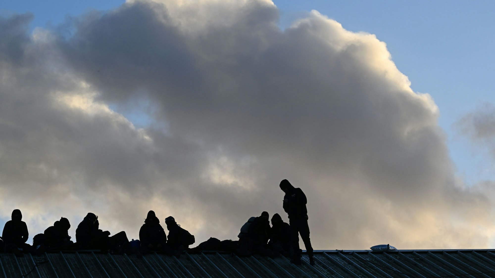 11.01.2023, Nordrhein-Westfalen, Erkelenz: Demonstranten sitzen bei der Räumung des Dorfes Lützerath auf dem Giebel eines Daches.