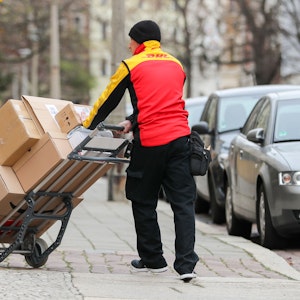 Ein DHL-Paketzusteller geht mit einer Sackkarre voller Pakete zu einem Haus.