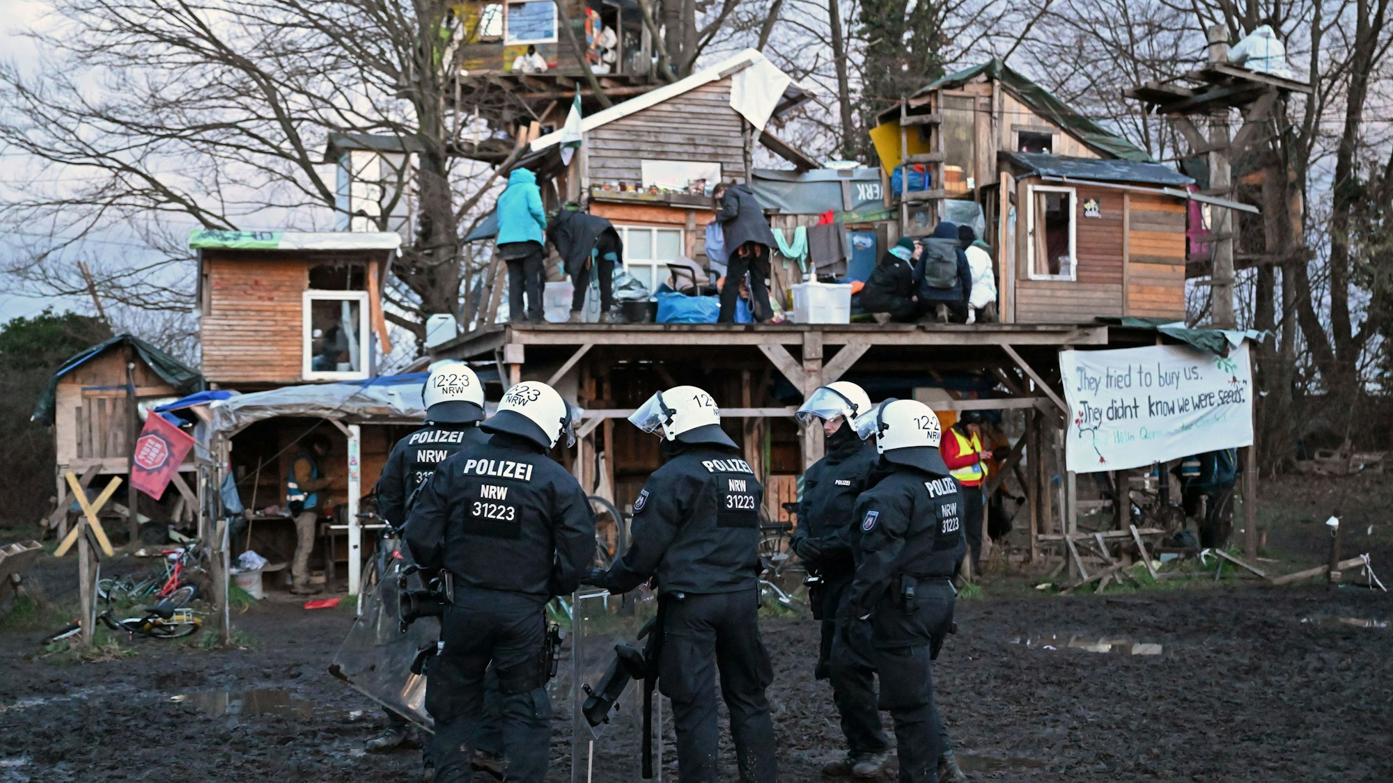 Polizisten stehen bei der Räumung von Lützerath vor Bretterhütten.