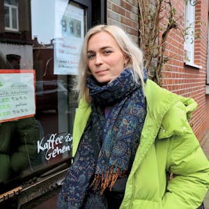 Nyke Slawik steht vor einem Leverkusener Café auf dem Bürgersteig und schaut in die Kamera.