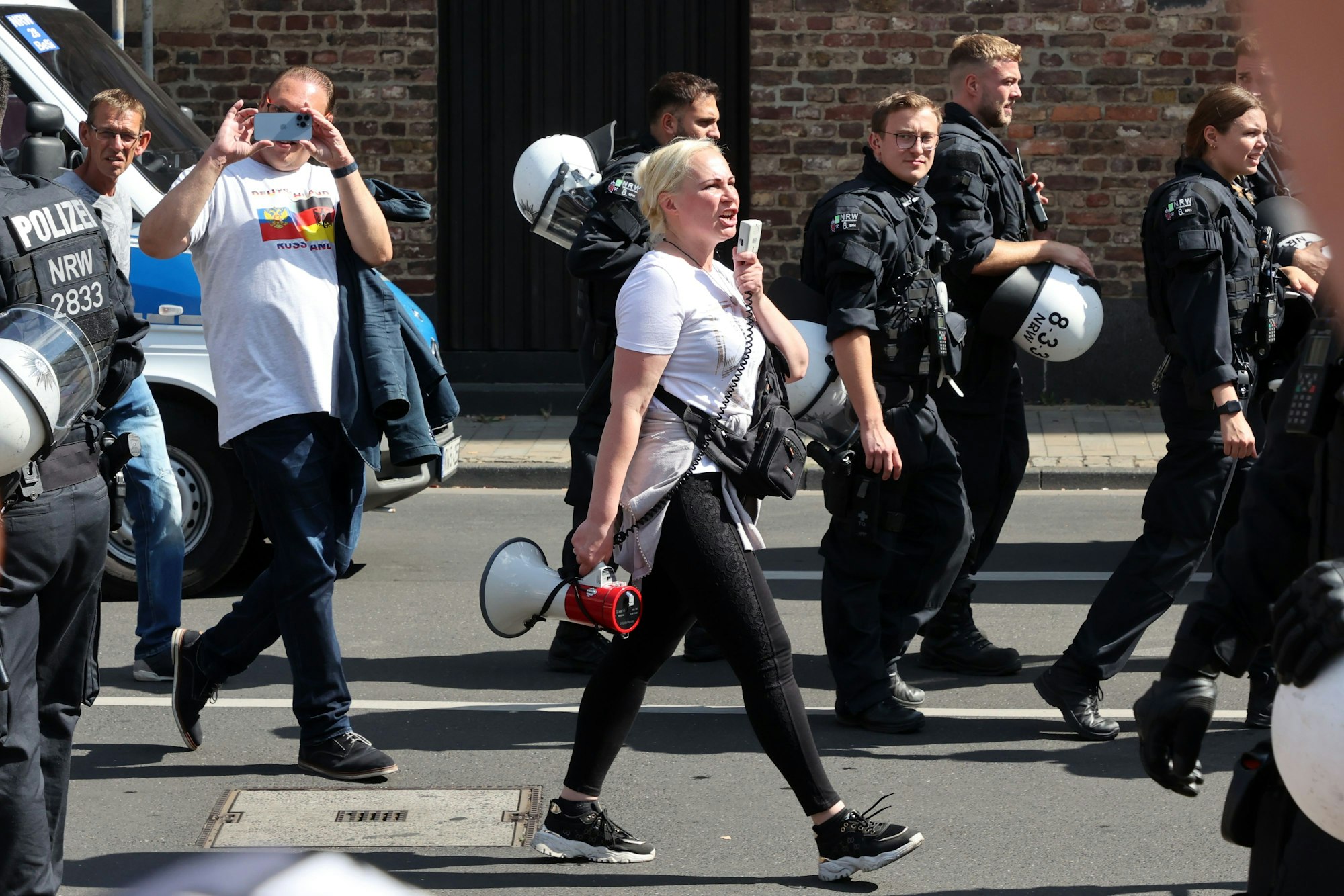 Kolbasnikova läuft mit einem Megafon in der Hand durch die Straßen. Um sie herum sind Polizisten.