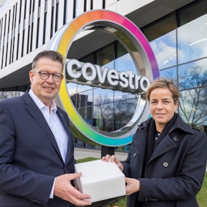 Produktionsvorstand Klaus Schäfer zeigt NRW-Wirtschaftsministerin Mona Neubaur vor der Covestro-Zentrale einen Würfel aus recyceltem Schaumstoff