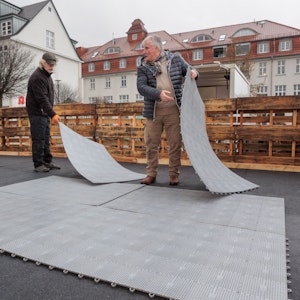 Zwei Männer bauen eine Kunststoffbahn aus mehreren Matten auf.
