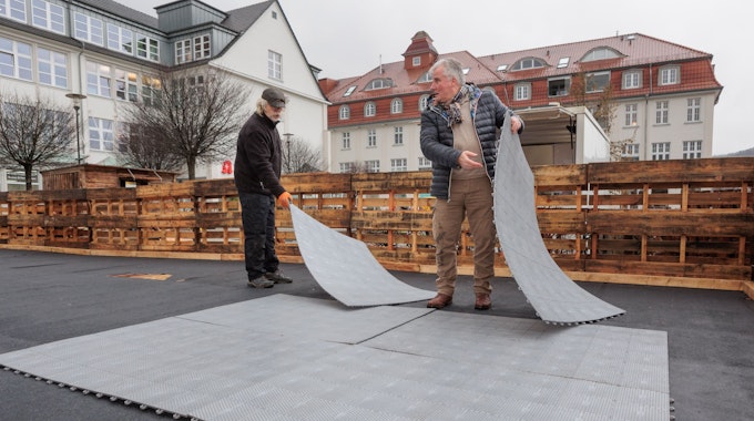 Zwei Männer bauen eine Kunststoffbahn aus mehreren Matten auf.