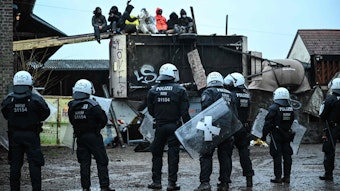 Polizisten stehen am zweiten Räumungstag vor Teilen eines alten Bauernhofs, Aktivisten protestieren auf dem Gebäude.