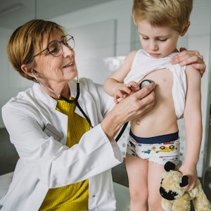 Eine Kinderärztin untersucht einen kleinen Jungen mit dem Stethoskop.