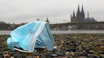 Eine weggeworfene Maske liegt am Rheinufer auf dem Boden.
