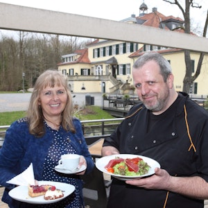 Marlene Jablonski-Reichelt und ihr Koch Mario Arke stehen neben Schloss Eulenbroich und halten Teller mit Essen darauf in den Händen.