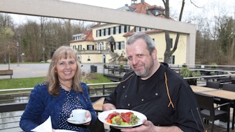 Marlene Jablonski-Reichelt und ihr Koch Mario Arke stehen neben Schloss Eulenbroich und halten Teller mit Essen darauf in den Händen.