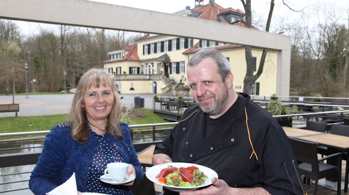 Marlene Jablonski-Reicheltsteht mit Koch Mario Arke vor dem Schloss und hält Teller mit Gerichten darauf in der Hand.
