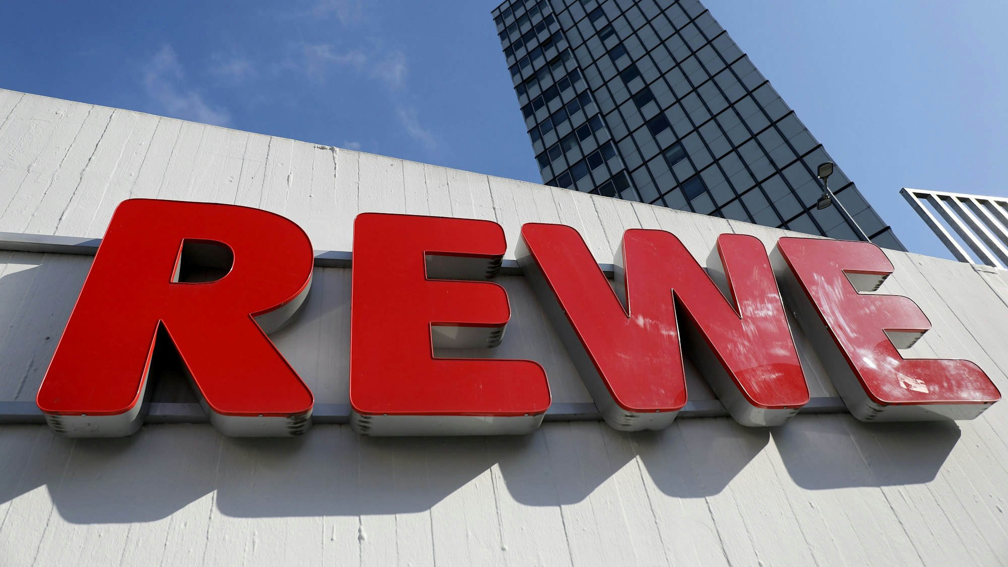 Das Rewe-Logo steht in roten Buchstaben auf einer Fassade.