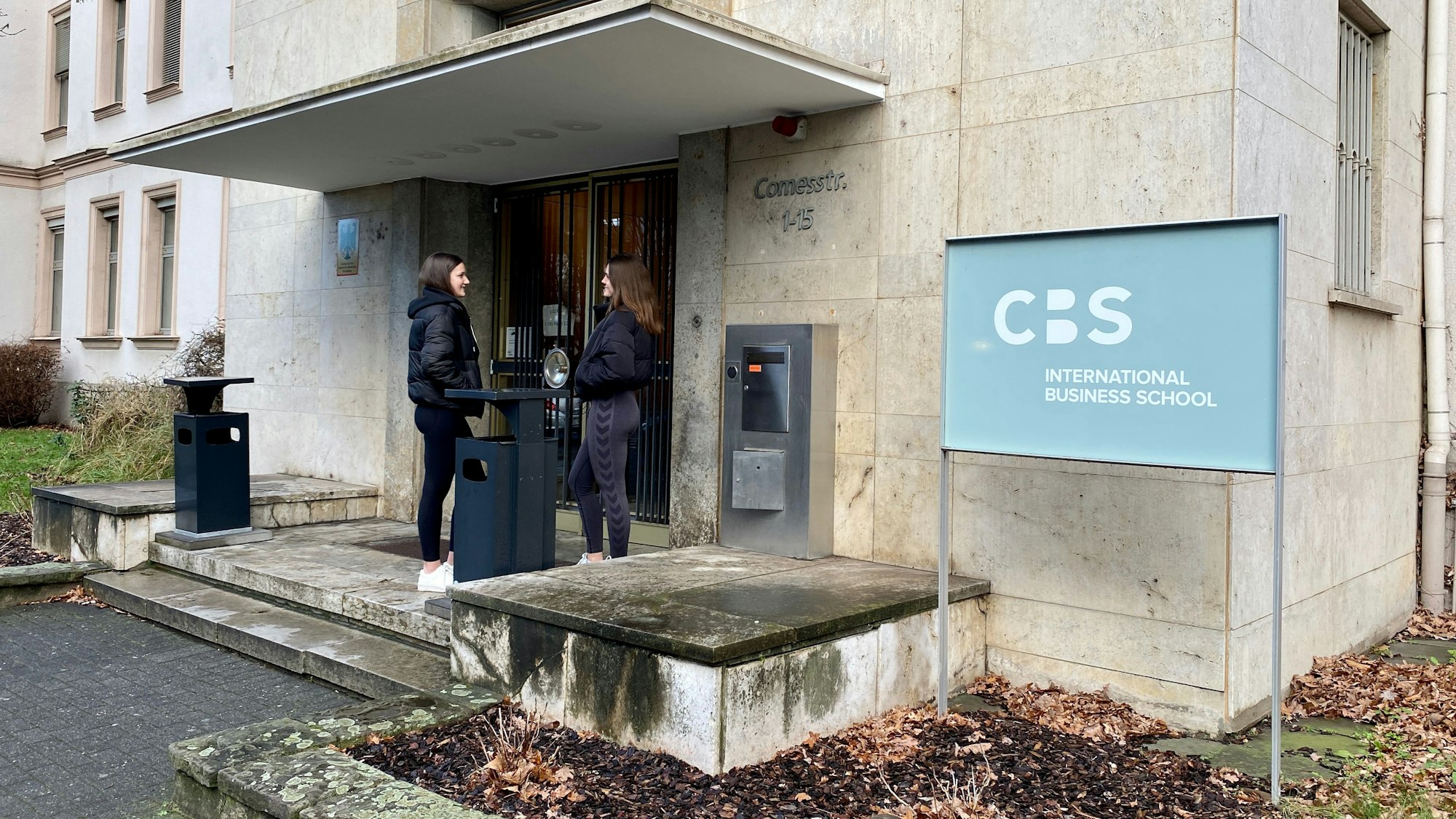 Zwei Studierende stehen vor dem Eingang der Cologne Business School.