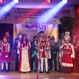 Vier Kinder in rot-weißen Karnevalstrachten stehen auf der Bühne. Hinter ihnen sind noch einige Erwachsene im Kostüm zu sehen.