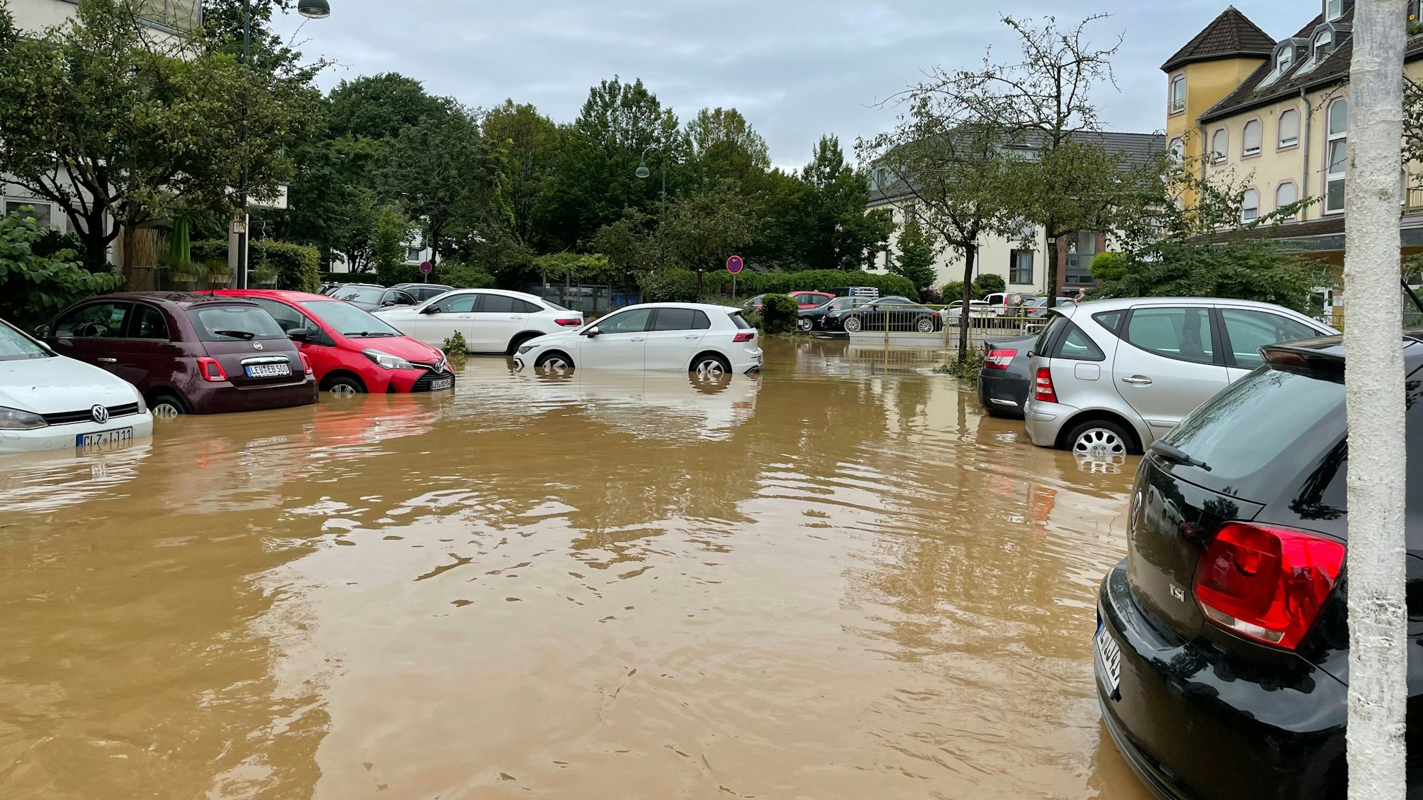 Autos stehen nach dem Hochwasser in einem See aus braunem Wasser..
