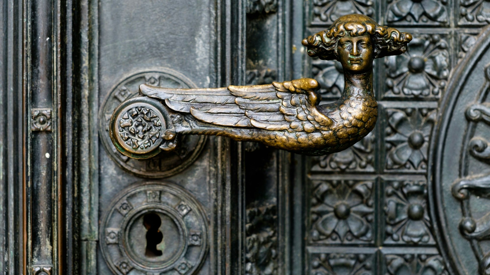 Das Bild zeigt einen bronzenen Türgriff in Form eines Engels mit Lockenkopf am Kölner Dom.