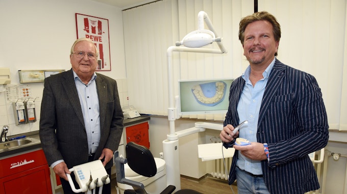 Die Doktoren Wilfried und Sascha Bonness stehen in einem Behandlungszimmer in ihrer Zahnarztpraxis und zeigen moderne medizinische Technik.