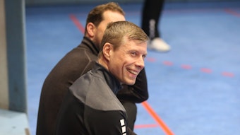 VfL-Trainer Gudjon Valur Sigurdsson sitzt auf einer Bank am Randes des Handballspielfeldes und lacht.