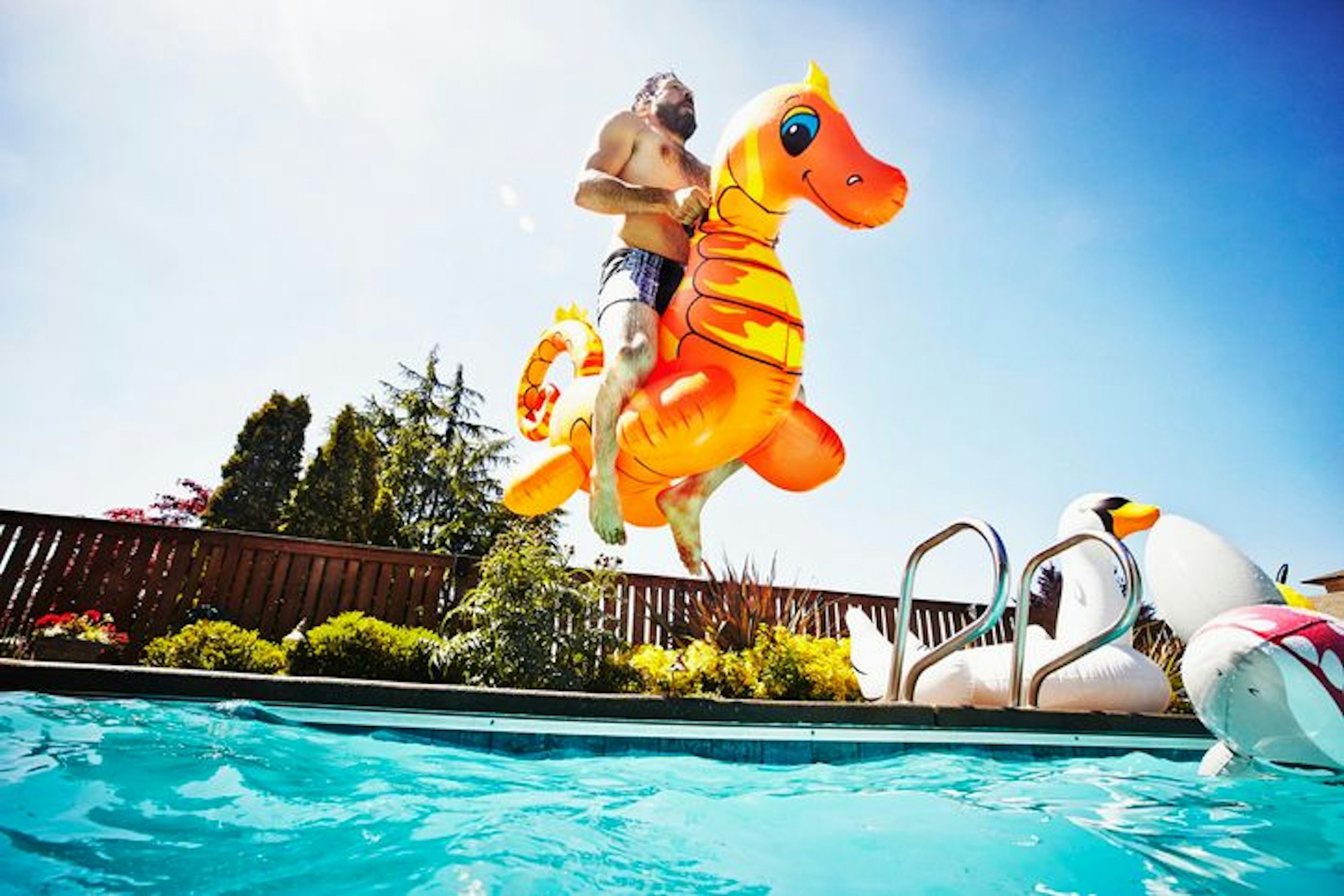 Mann springt auf einem aufblasbaren Seepferdchen-Spielzeug in den Pool an einem heißen Tag