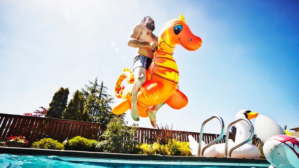 Mann springt auf einem aufblasbaren Seepferdchen-Spielzeug in den Pool an einem heißen Tag