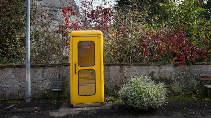 Eine gelbe Telefonzelle steht am Rande einer Straße. 