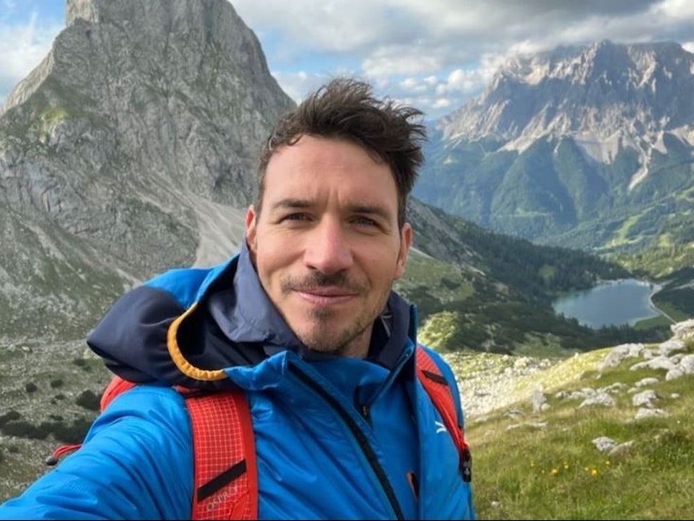 Felix Neureuther macht ein Selfie vor einer Bergkulisse.