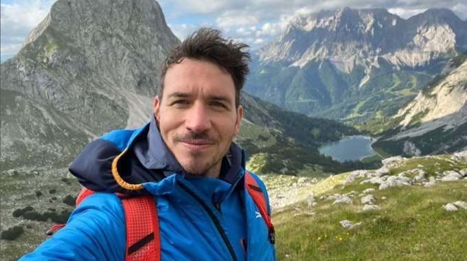 Felix Neureuther macht ein Selfie vor einer Bergkulisse.