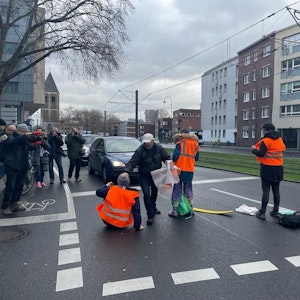 Ein Mann mit grauer Jacke greift Klimaaktivisten mit orangen Warnwesten bei einer Straßensperre in der Kölner Innenstadt an.